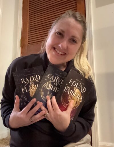 woman who is excited holding all three paperback books in the Astrid Stone trilogy